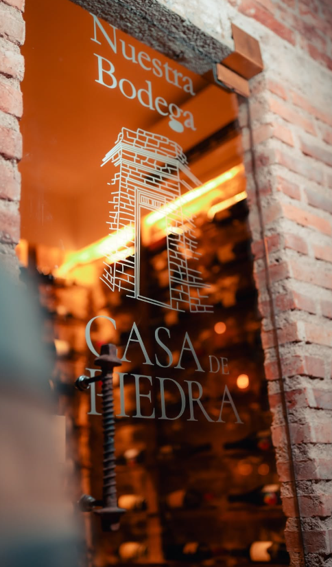 Puerta de vidrio de Nuestra Bodega con el grabado de Casa de Piedra y el interior iluminado al fondo